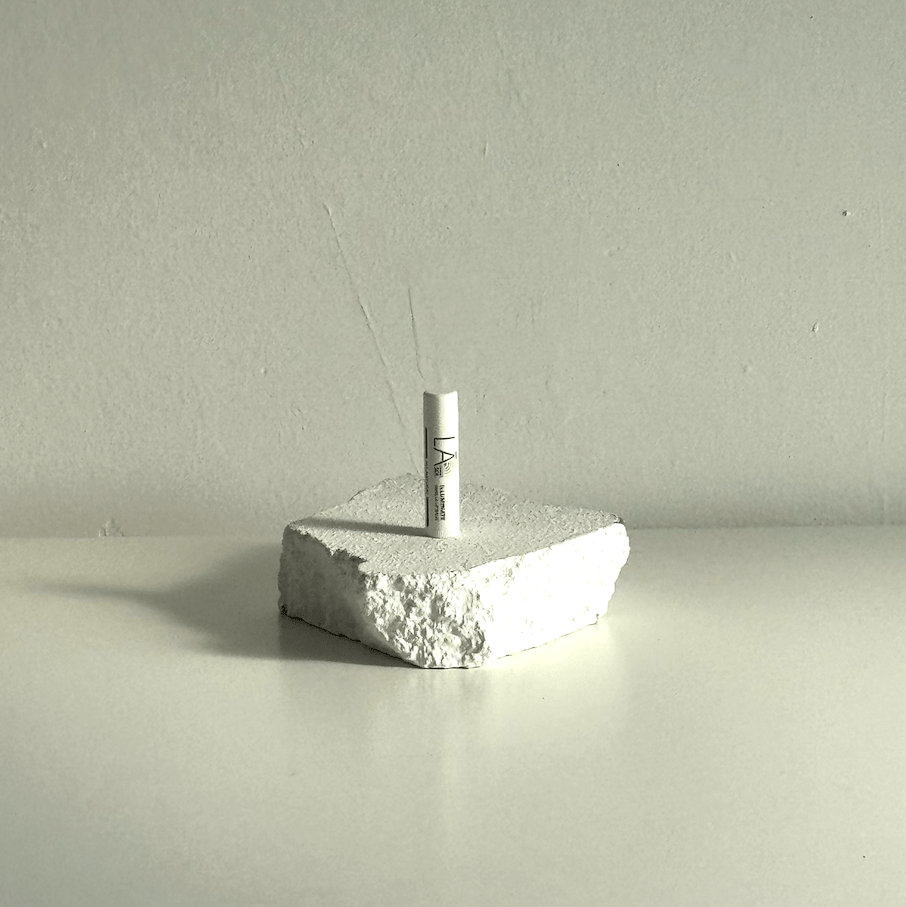 A small white cylindrical item standing upright on a rough, textured white stone-like block against a plain light gray wall and surface.