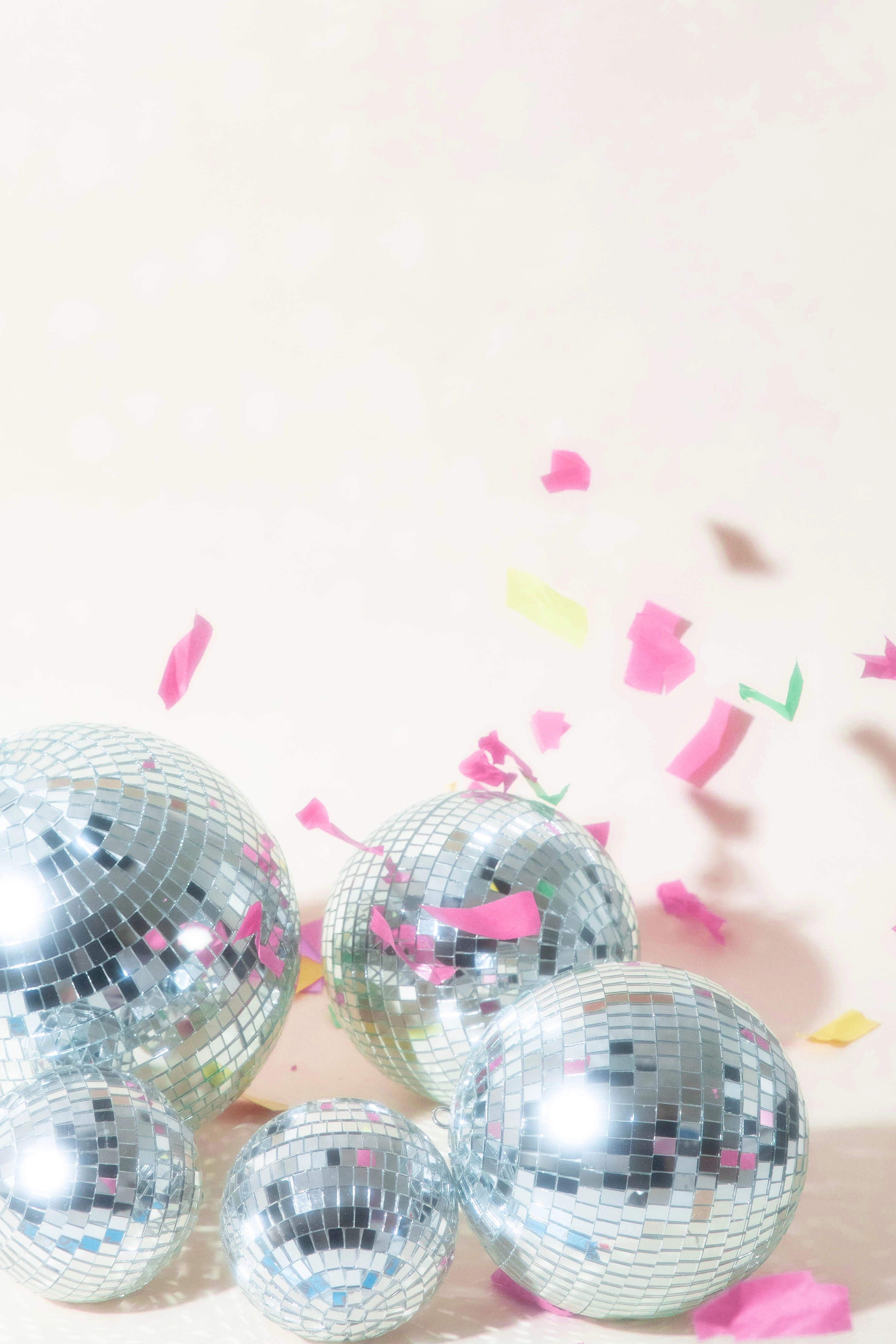 Several disco balls on a light pink background with pink, green, and yellow confetti