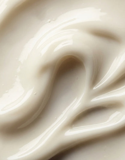 A close-up texture shot of a thick, creamy off-white toothpaste product with smooth, glossy swirls.