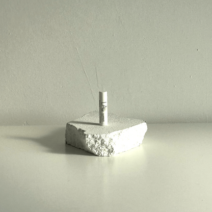 A small white cylindrical item standing upright on a rough, textured white stone-like block against a plain light gray wall and surface.