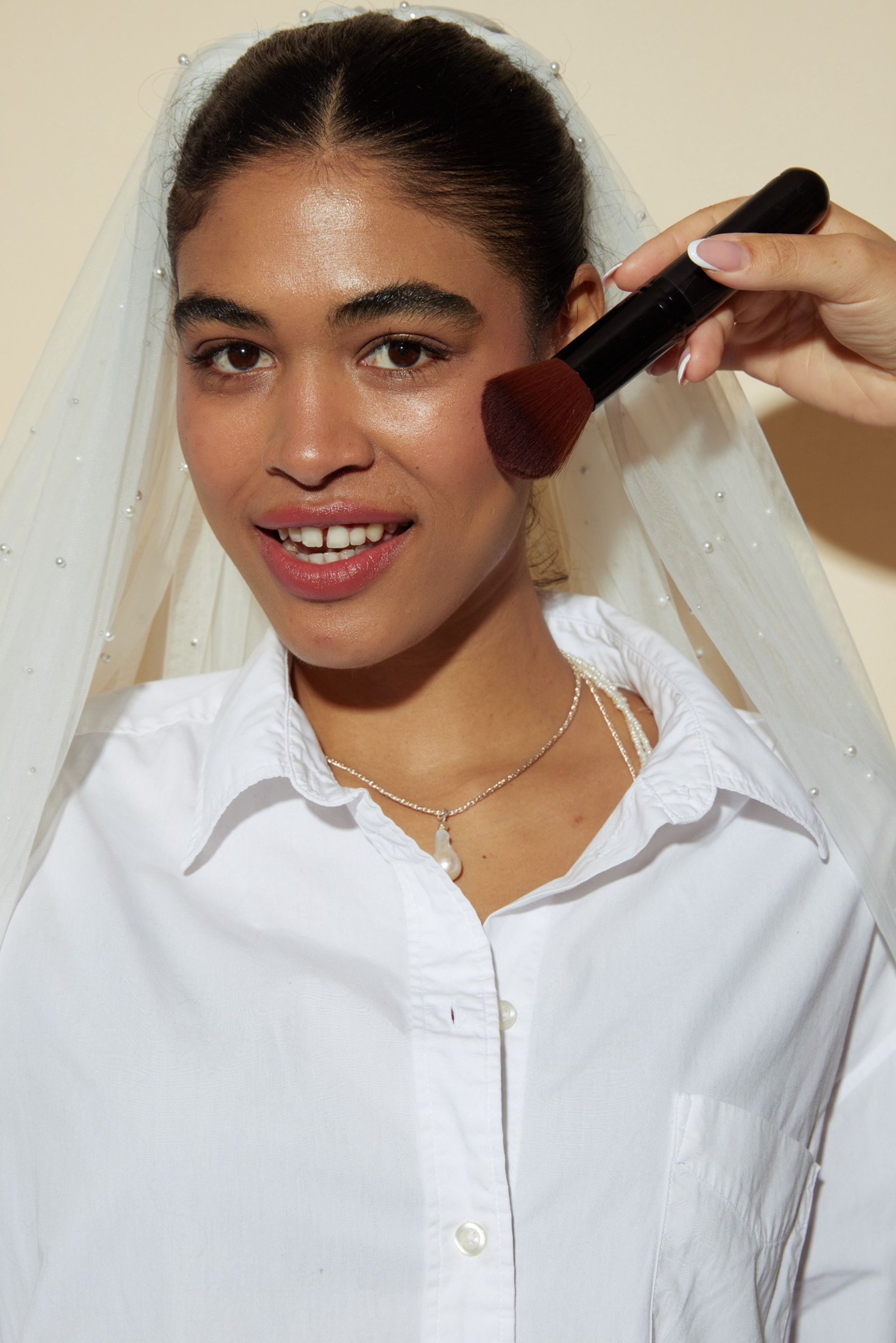 Person applying makeup with a brush, wearing a white shirt and veil.