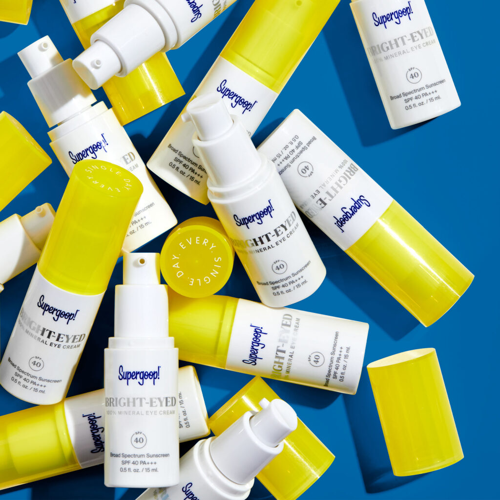 a bunch of supergoop eye creams laying on a blue table
